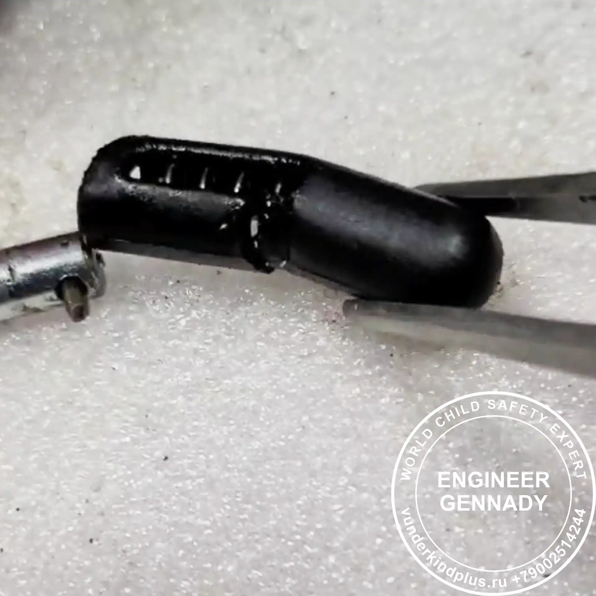 Tweezers holding a small broken plastic capsule with a spring inside.